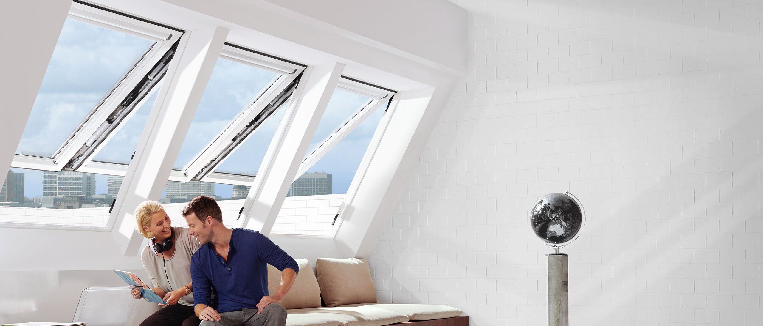 Ein Mann und eine Frau sitzen in einem Zimmer. Drei offene Dachfenster sind hinter ihnen zu sehen.