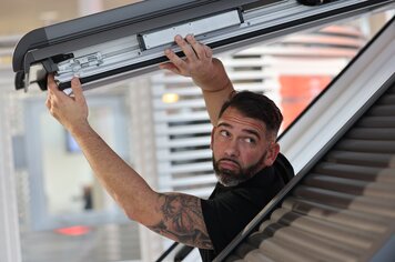 Ein Mann der aus einem offenen Dachfenster herausragt und den Fensterflügel des offenen Dachfensters nach oben drückt. 